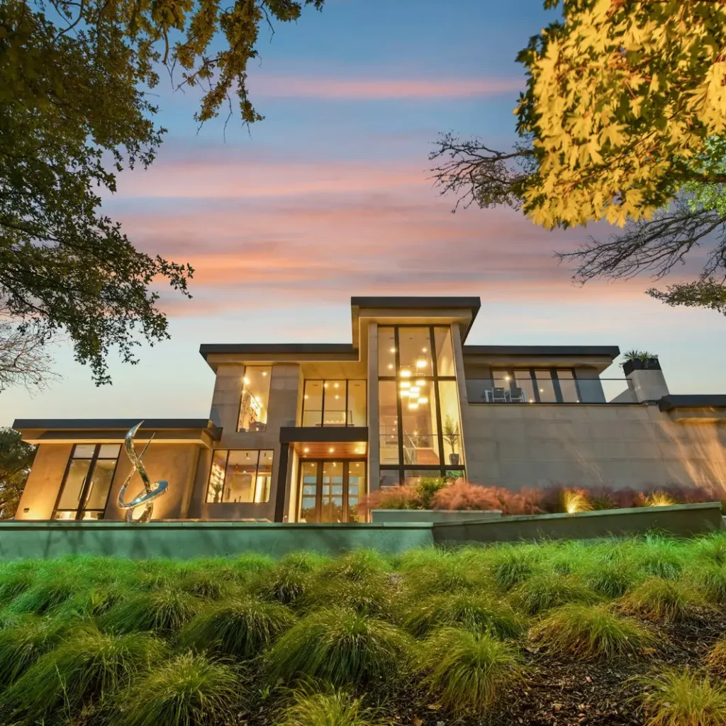 A finished modern custom home at dusk, its windows lit warmly
