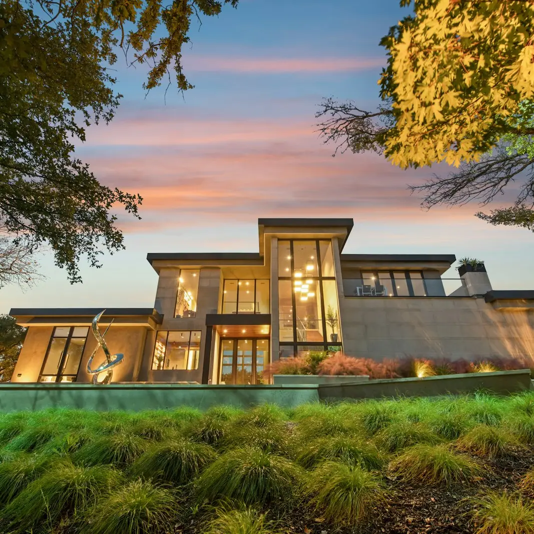 A finished modern custom home at dusk, its windows lit warmly